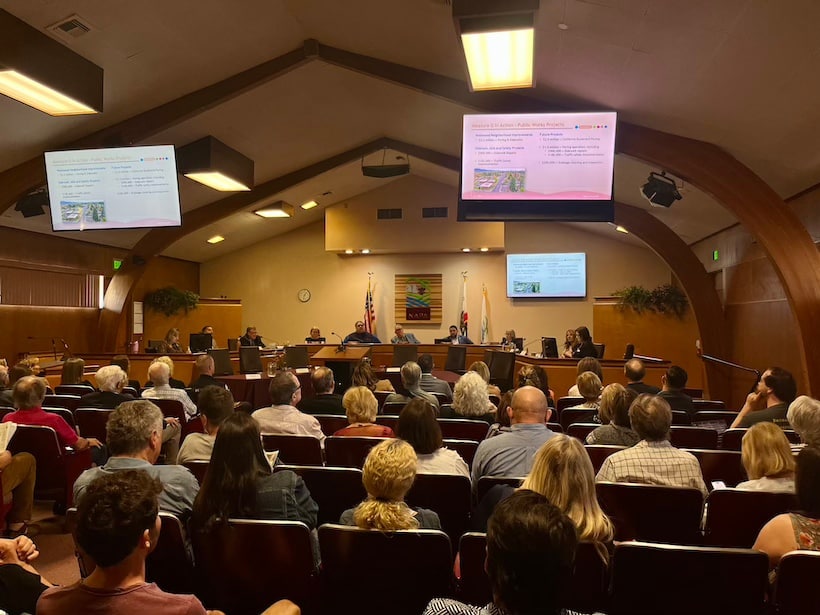 crowd seated in a room facing a panel of city officials 