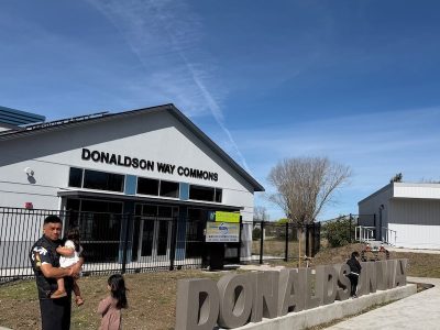 man standing in front of building holding baby and kid