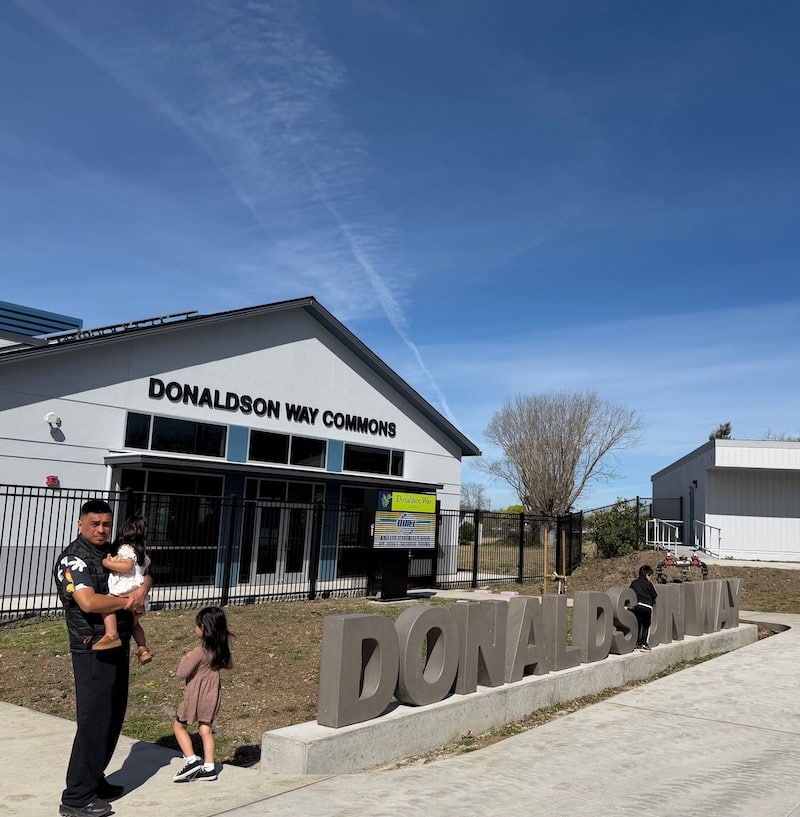 man standing in front of building holding baby and kid