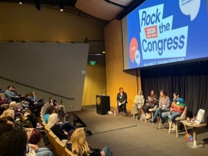people on a stage speaking to an audience in lecture hall bleachers