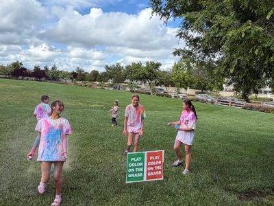 four girls and a child running around a lawn covered in colors